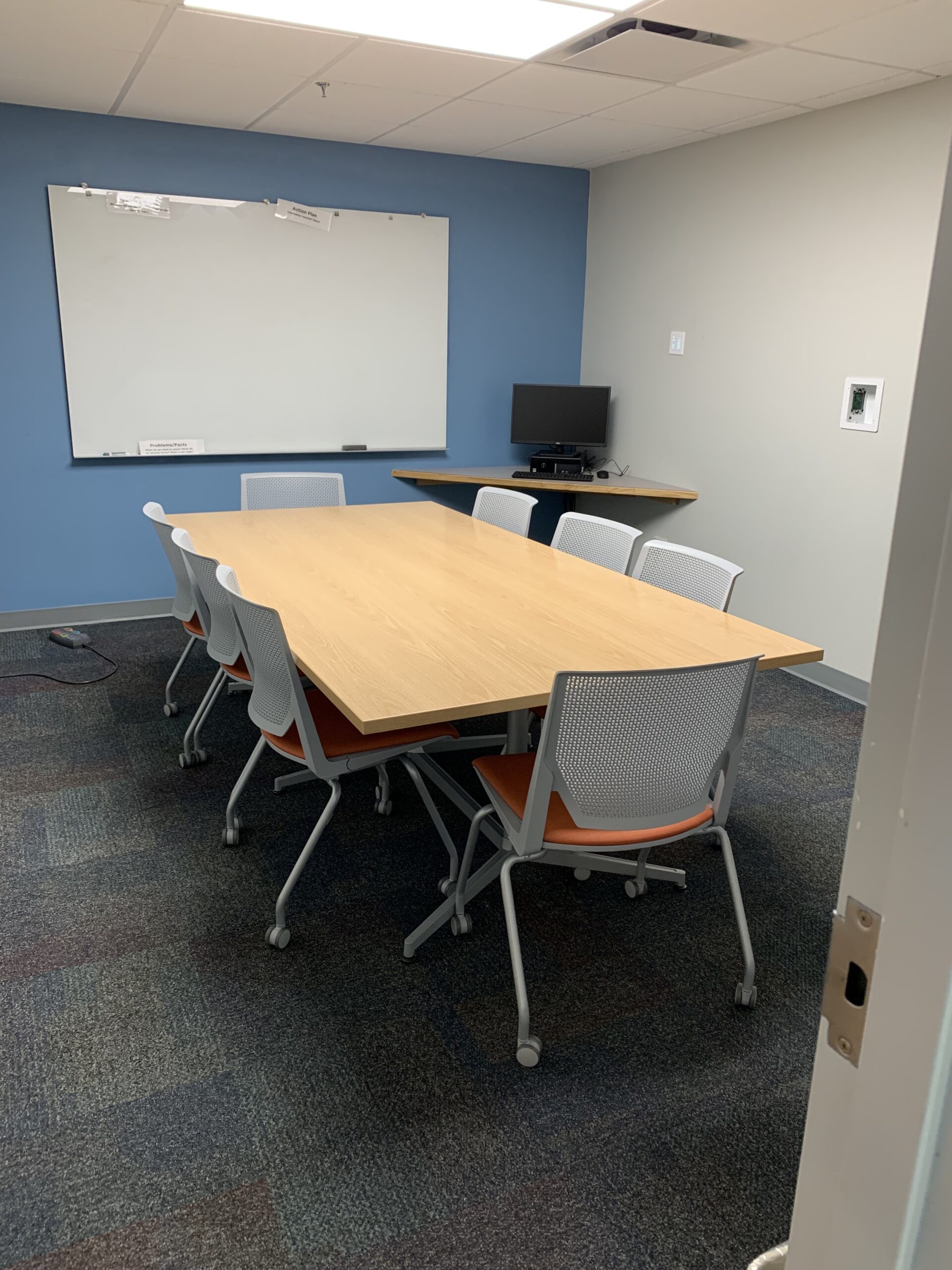 table with 8 chairs. White boards are on the walls surrounding it.